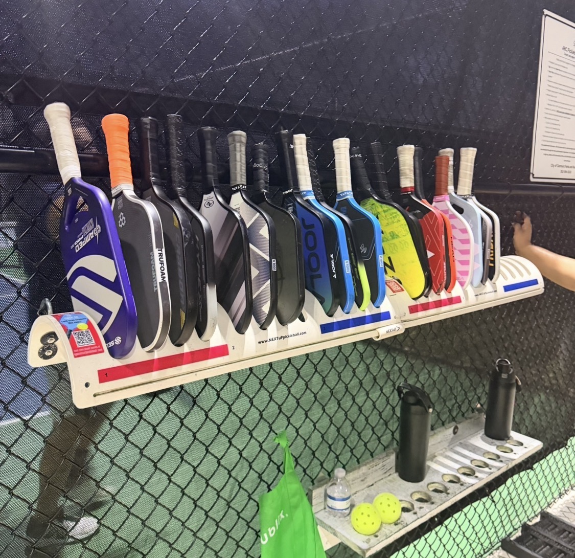 A crowded pickleball court's paddle rack, stacked with paddles waiting their turn for the next game
